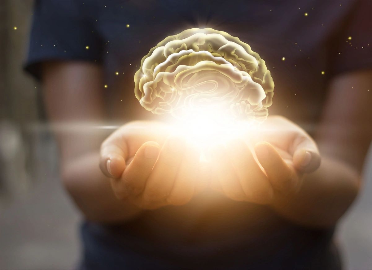Cupped hands holding a softly lit illustration of a brain.
